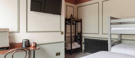 A hotel room with a bunk bed, a desk with a chair, a radiator, and a television mounted on the wall.