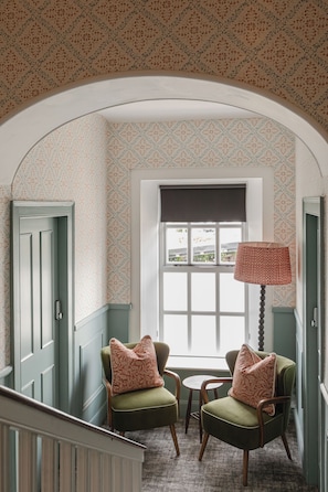 A room with two green armchairs, a small table, and a lamp. There is a window with a view outside. - Avoca House (Newcastle)