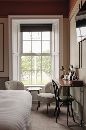 A hotel room with a bed, two chairs, a small table, and a desk with a lamp.