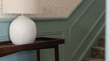 Un escalier recouvert d’une moquette à motifs et une lampe blanche posée sur une console en bois.