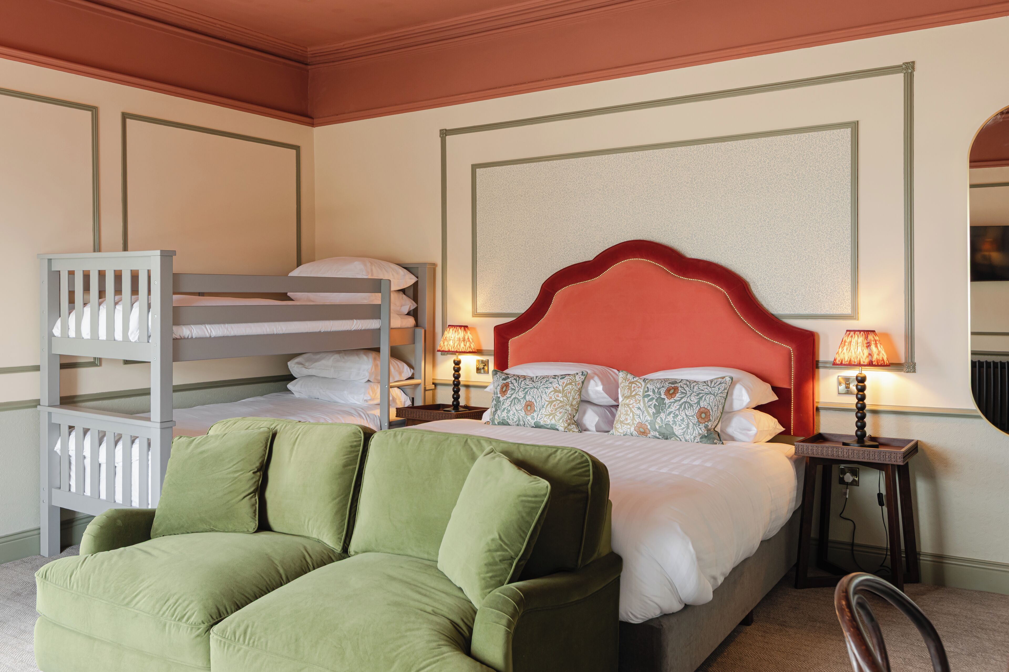 Habitación de hotel con literas, un sillón verde, dos mesitas de noche con lámparas y una obra de arte enmarcada grande en la pared.