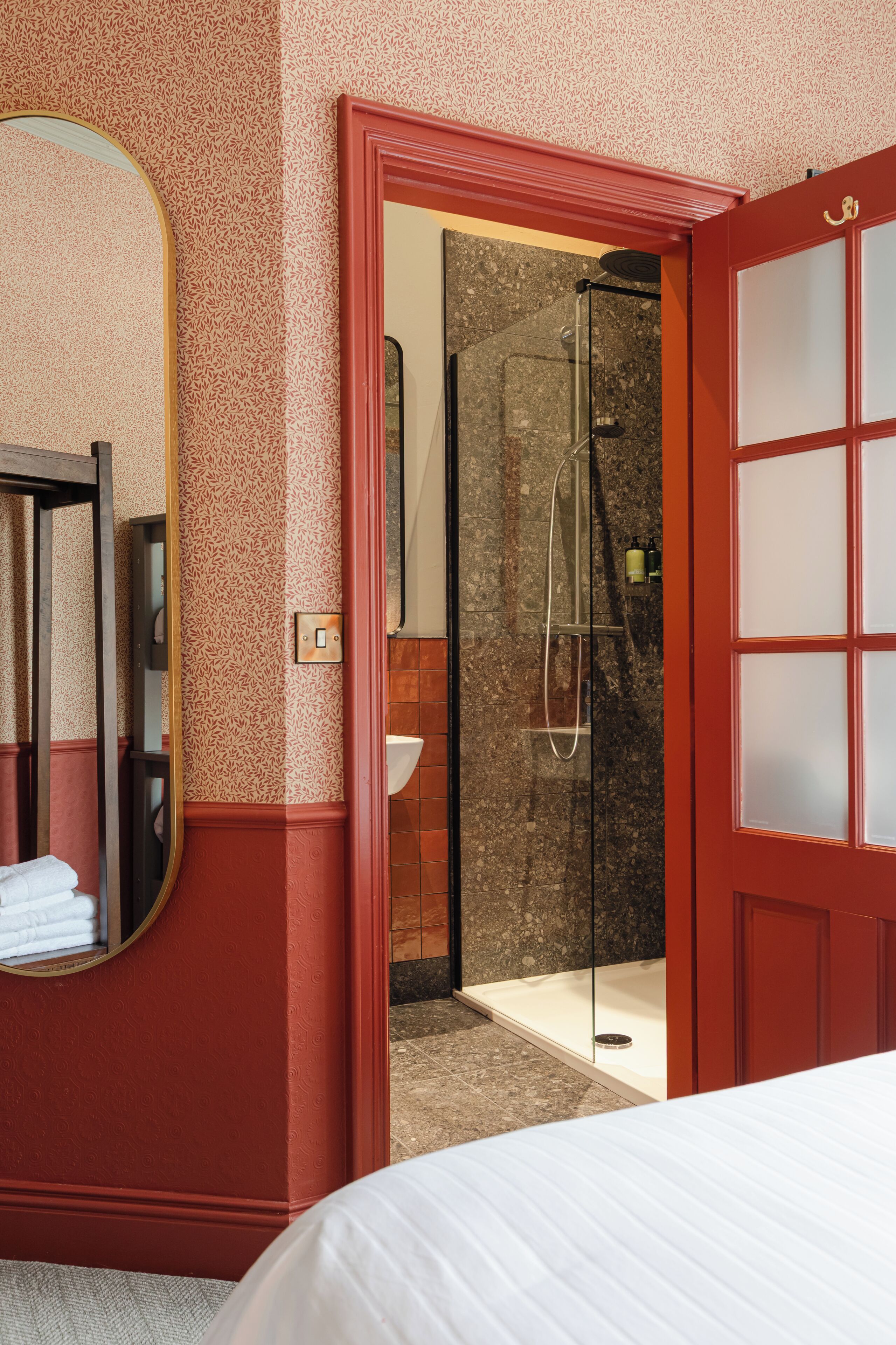 Habitación de hotel con una cama grande, un espejo, zona de ducha y una puerta roja.