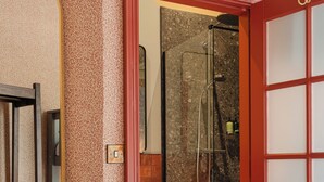 A hotel room with a large bed, a mirror, a shower area, and a red door. - Avoca House (Newcastle)
