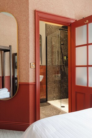 A hotel room with a large bed, a mirror, a shower area, and a red door.