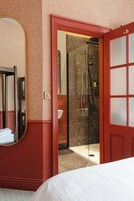 Habitación de hotel con una cama grande, un espejo, zona de ducha y una puerta roja.