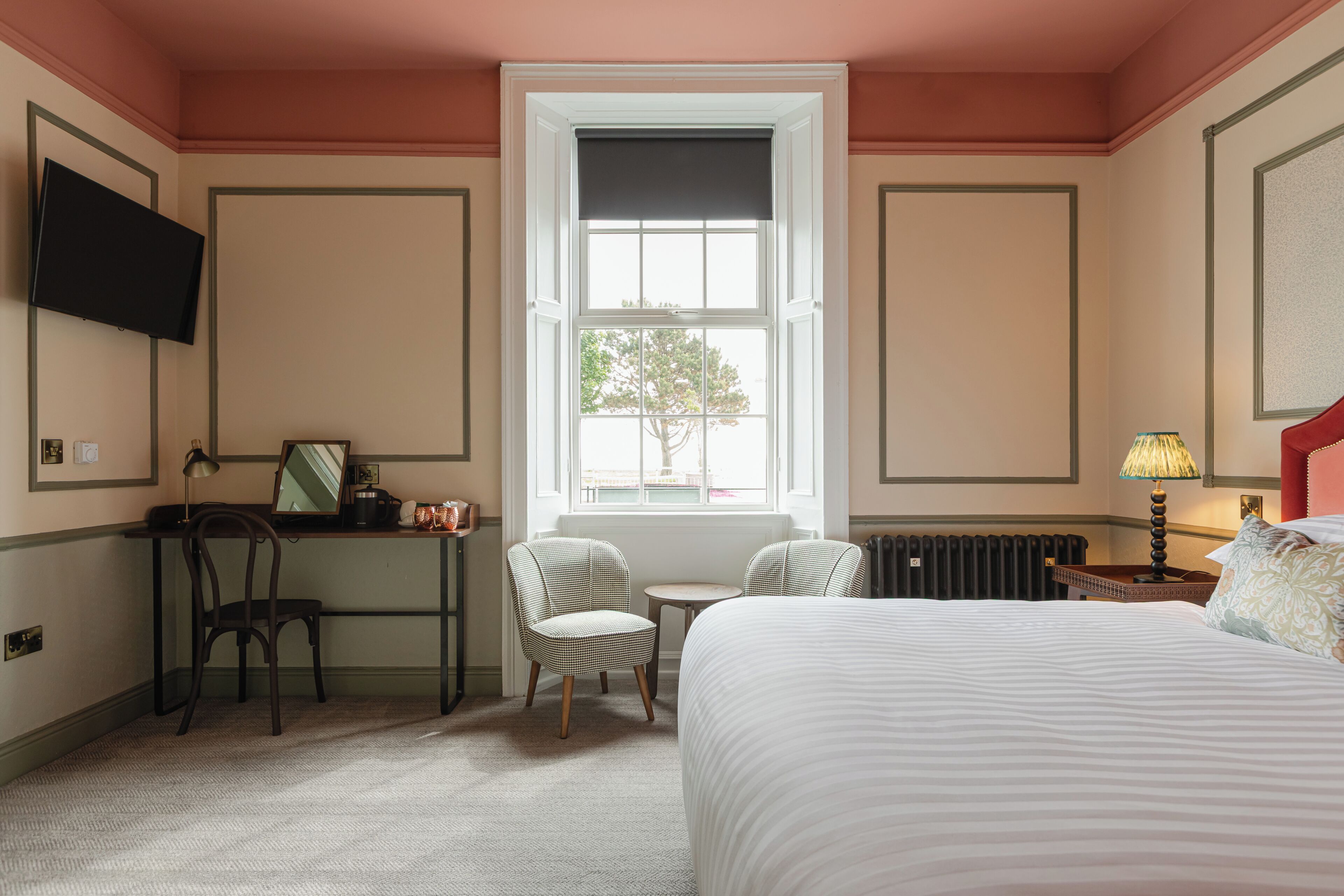 Une chambre d’hôtel équipée d’un lit, d’un bureau, d’une chaise, d’une télévision, d’une fenêtre donnant sur un paysage agréable et d’un radiateur.