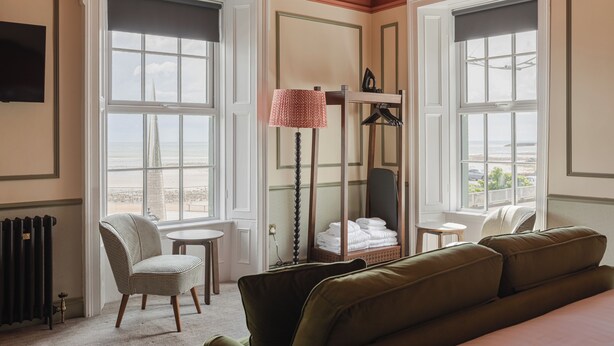 A hotel room with a large window, a chair, a table, a sofa, and a radiator. - Avoca House (Newcastle)