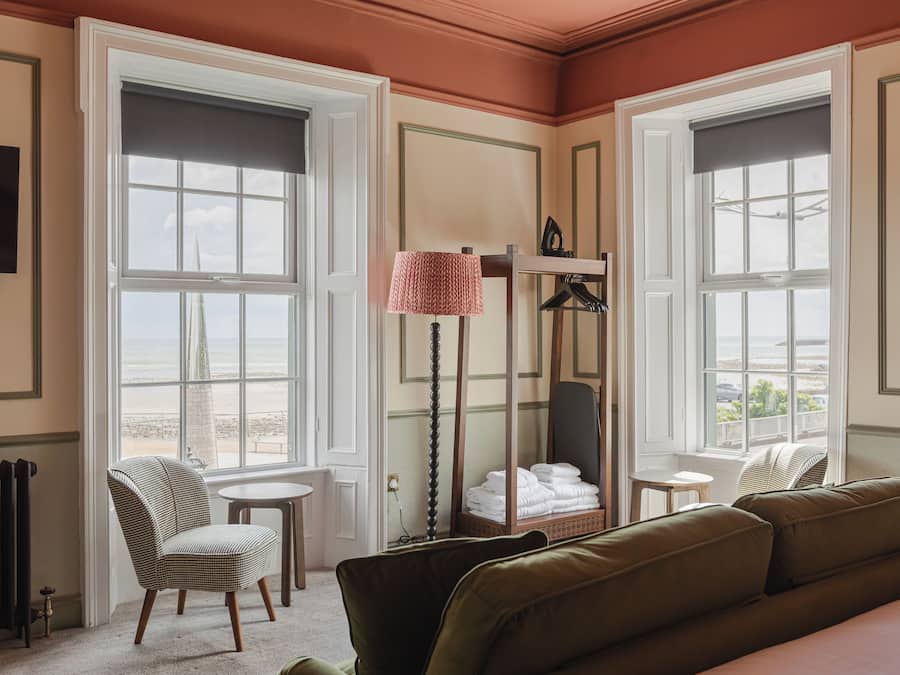 Habitación de hotel con un ventanal grande, una silla, una mesa, un sofá y un radiador.