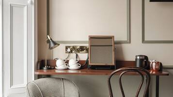 A hotel room with a round wooden table, a houndstooth patterned ottoman, a wooden chair, a desk with a lamp, a telephone, and a framed picture on the wall.