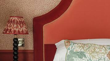 Una habitación de hotel con un cabecero rojo, una lámpara estampada y una almohada con motivos florales.