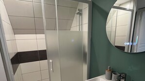 Une salle de bain moderne avec une douche à parois de verre, un lavabo blanc avec un miroir et un mur d’accent vert.