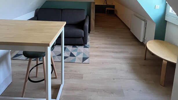Une pièce de style loft avec un plafond haut, un canapé, une table à manger et un petit tabouret.
