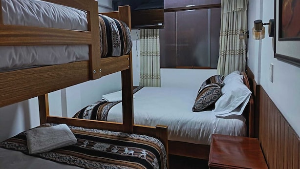 Una stanza con letti a castello, un letto singolo, un tavolino, una lampada e una finestra con tende.