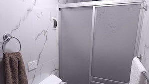 Un bagno con doccia, un porta asciugamani con un asciugamano marrone e un asciugamano bianco su uno scaffale.