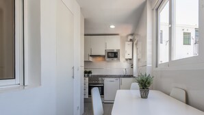 A compact kitchen with white cabinets, a microwave, and a dishwasher. There is a dining table with chairs and a potted plant. - Flat Near Las Ventas District (Madrid)