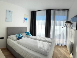 Una habitación de hotel moderna con una cama curvada, ropa de cama blanca y un ventanal con cortinas translúcidas.