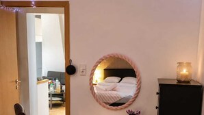 Une chambre à coucher avec un lit, une commode, une chaise, un miroir et une petite table sur laquelle se trouve une bougie.