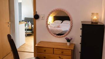 Une chambre à coucher avec un lit, une commode, une chaise, un miroir et une petite table sur laquelle se trouve une bougie.