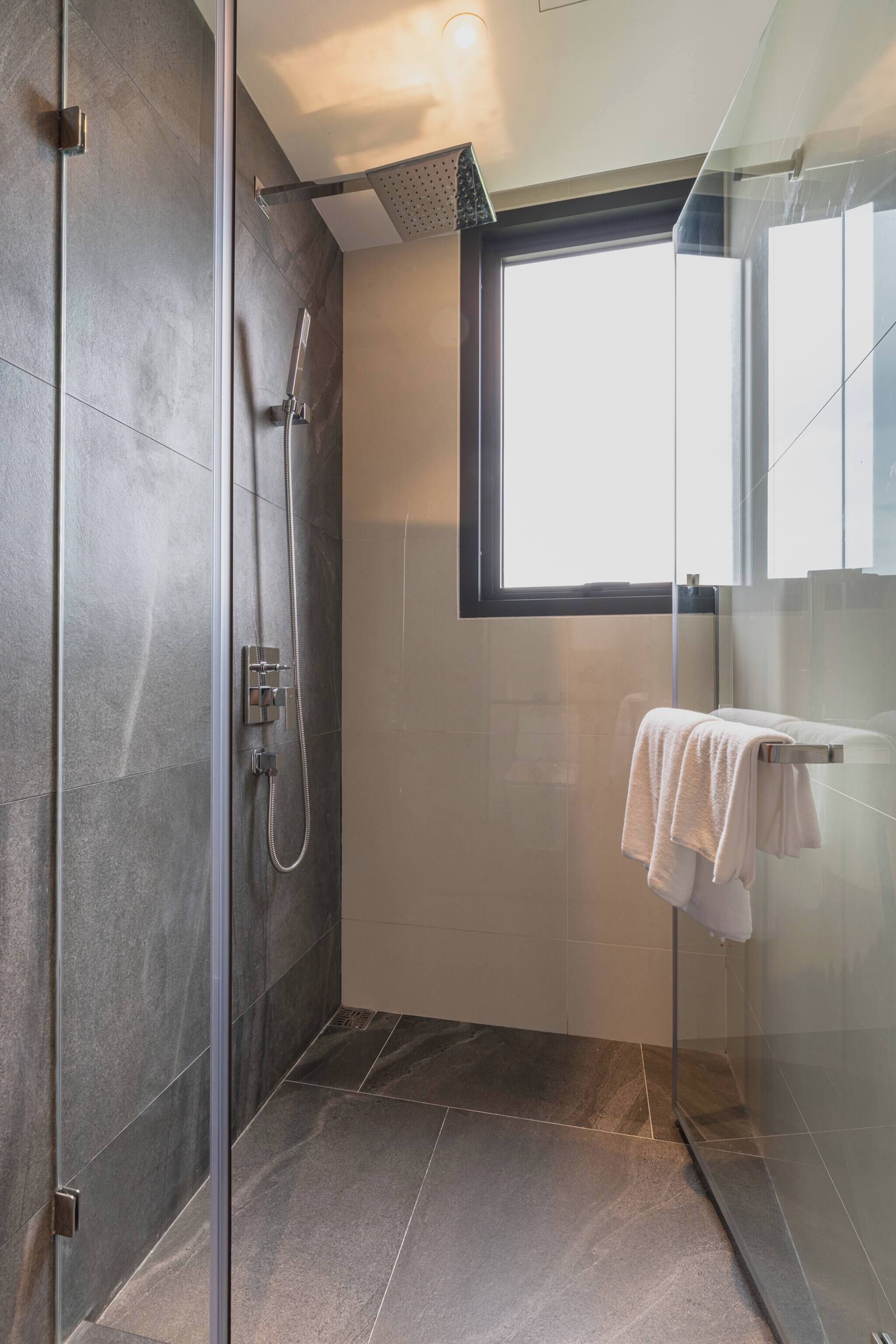 A modern bathroom with a glass shower enclosure, a window, and a towel rack.