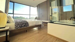 Una camera da letto moderna con un letto grande, un comodino, un bagno in vetro e vista sull'esterno.