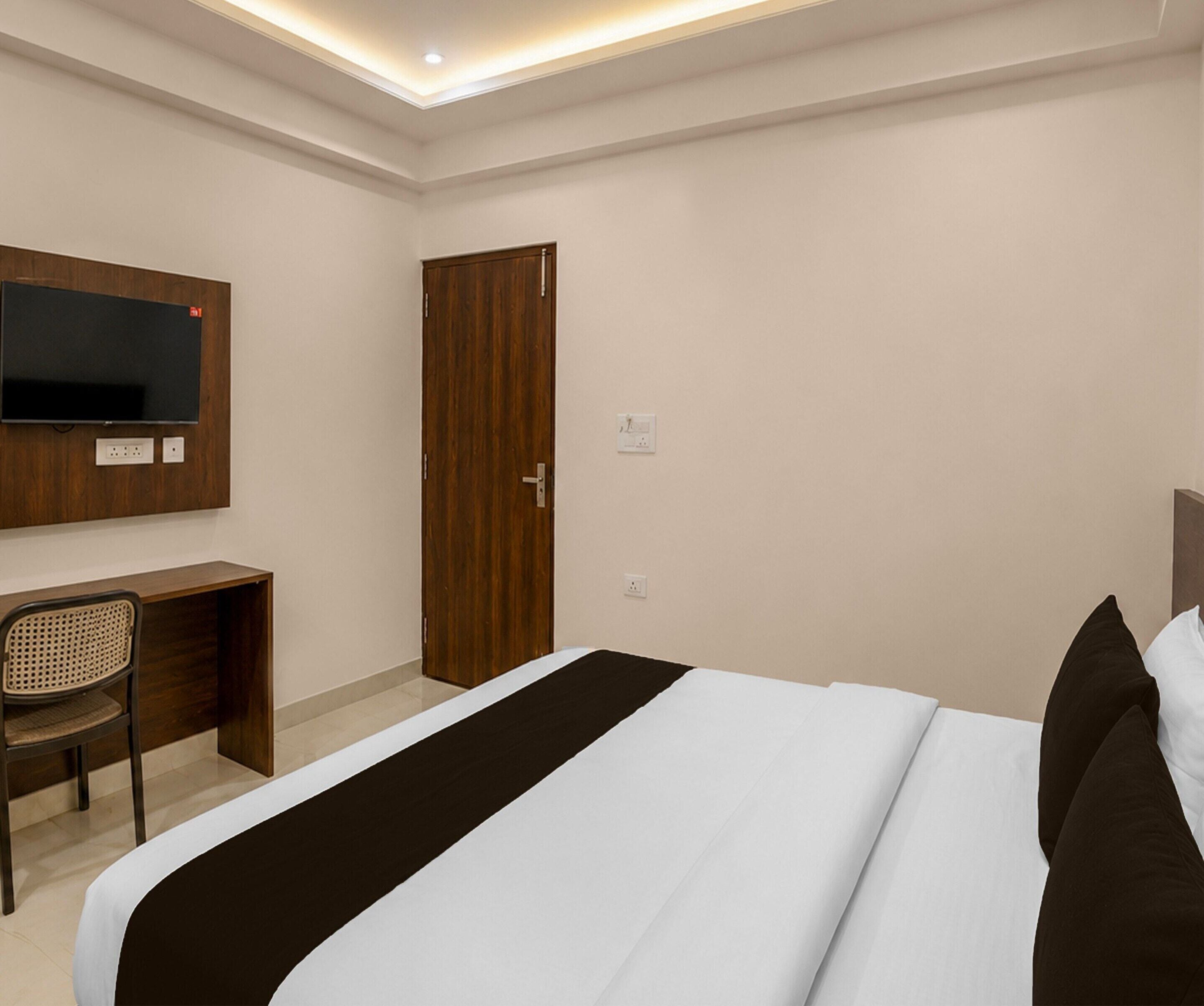 Une chambre d’hôtel comprenant un lit, un bureau, une chaise, un téléviseur fixé au mur et une porte.