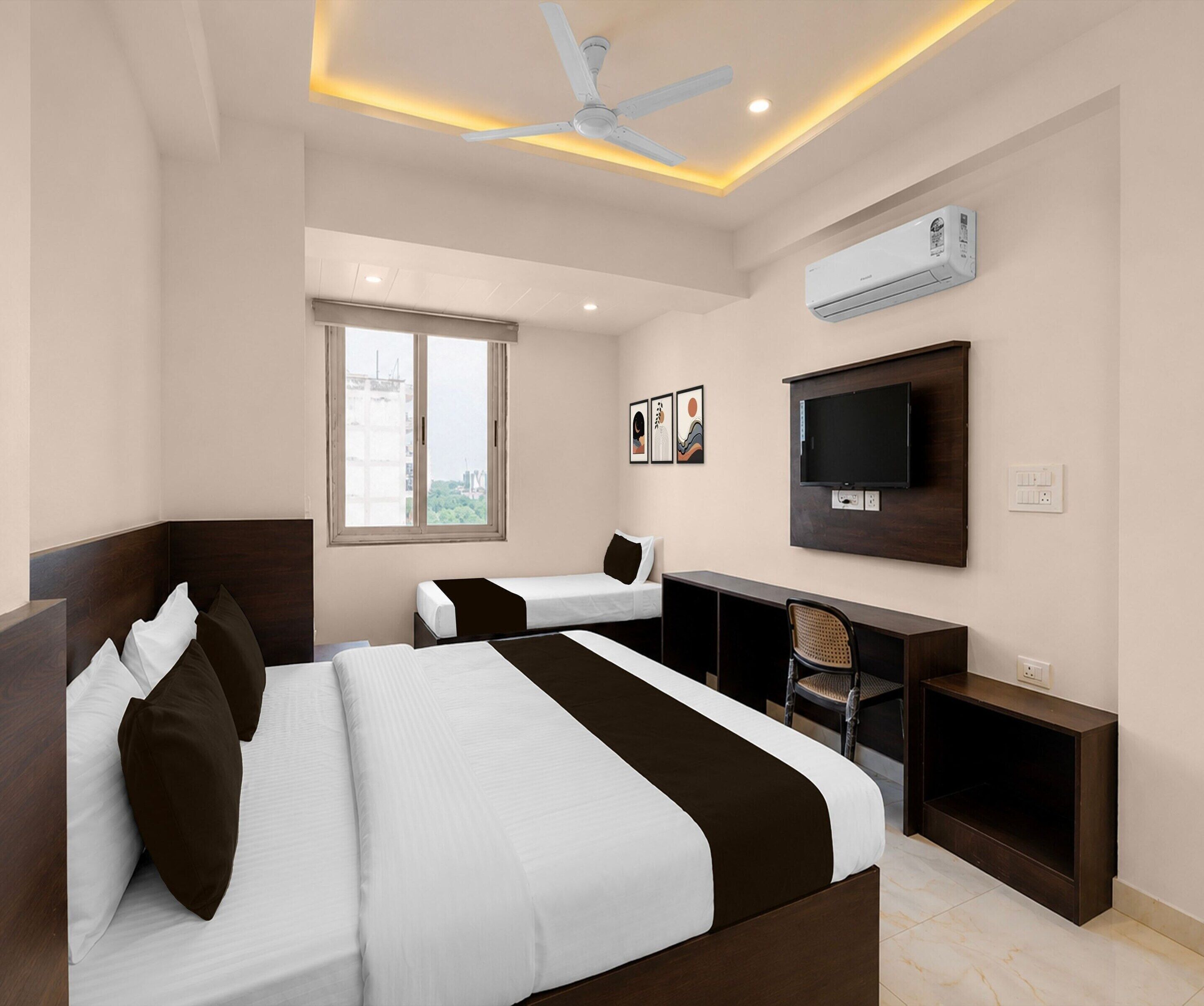 A hotel room with two beds, a desk, a chair, a TV, and an air conditioning unit.