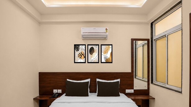 Habitación de hotel con cama, mesitas de noche, equipo de aire acondicionado, un ventanal grande y tres cuadros enmarcados en la pared.