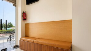 A bench with a wooden backrest and cushioned seat, a fire extinguisher mounted on the wall, and a television screen above.