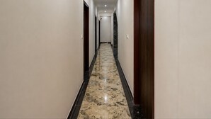 A hotel hallway with marble flooring, wooden doors, and a ceiling light.