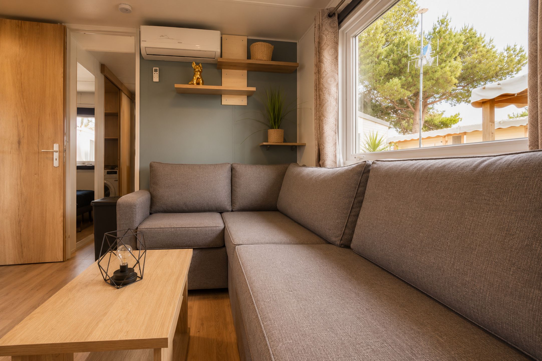 Ein zeitgemäßer Wohnbereich mit einer Couch, einem Holztisch und einem Fenster mit Blick auf Bäume.