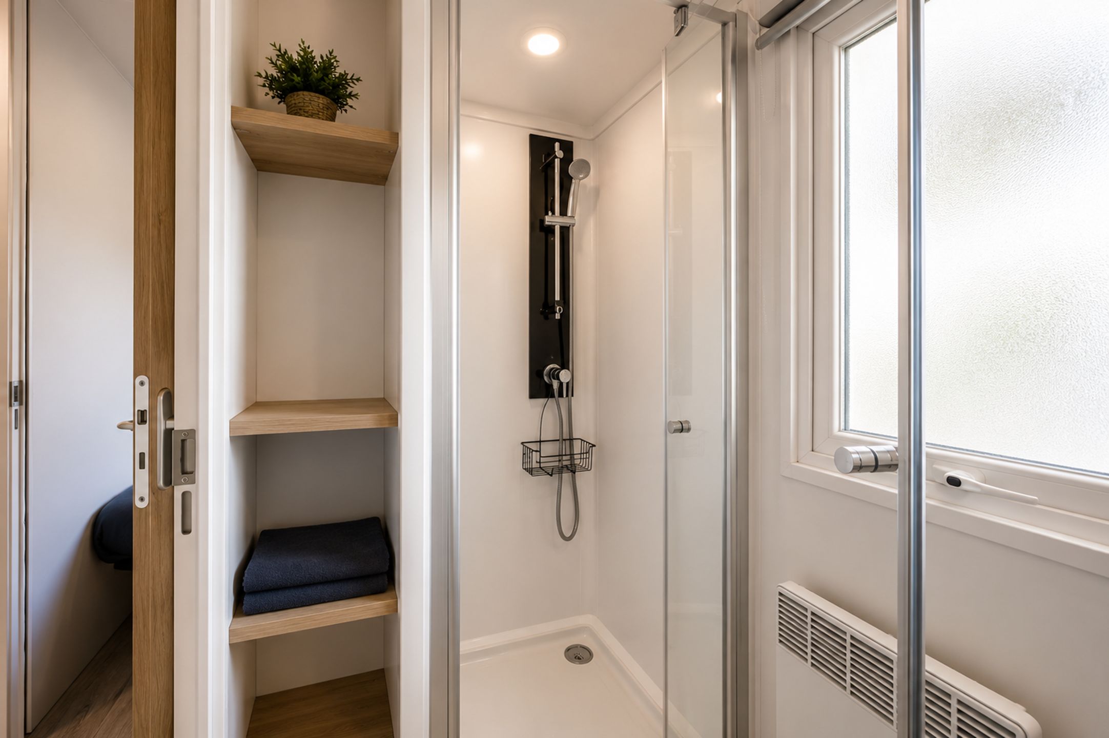 Eine bodenebene Dusche mit Glastür, ein Holzregal mit einer Pflanze und ein Fenster mit satiniertem Glas.