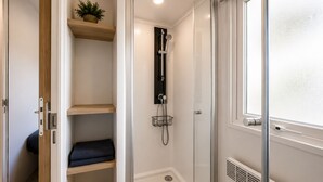 A walk-in shower with a glass door, a wooden shelf with a plant, and a window with frosted glass. - Le Cocon du Mar Estang - Terrace, air conditioning, sleeps 8 (Canet-en-Roussillon)