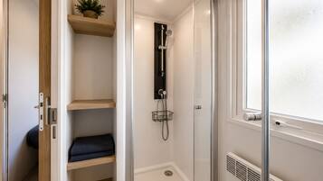 Eine bodenebene Dusche mit Glastür, ein Holzregal mit einer Pflanze und ein Fenster mit satiniertem Glas.
