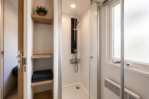 Une douche à l’italienne avec une porte en verre, une étagère en bois ornée d’une plante et une fenêtre à vitrage dépoli.
