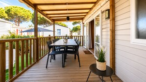 A covered outdoor deck with a table and chairs, a potted plant, and a view of neighboring houses. - Le Cocon du Mar Estang - Terrace, air conditioning, sleeps 8 (Canet-en-Roussillon)