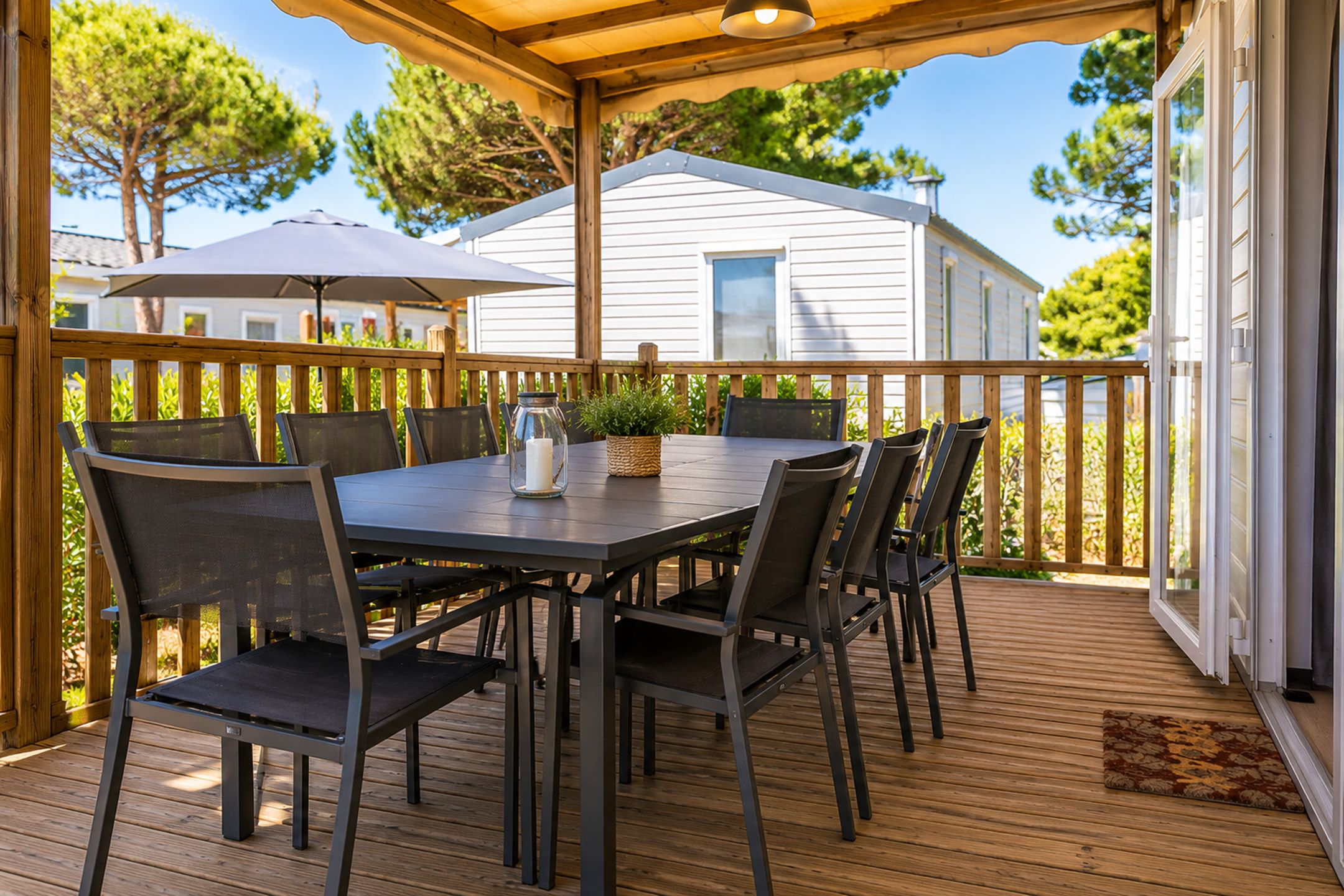 Een overdekt terras buiten met een tafel en stoelen, een houten terras en een uitzicht op een huis op de achtergrond.