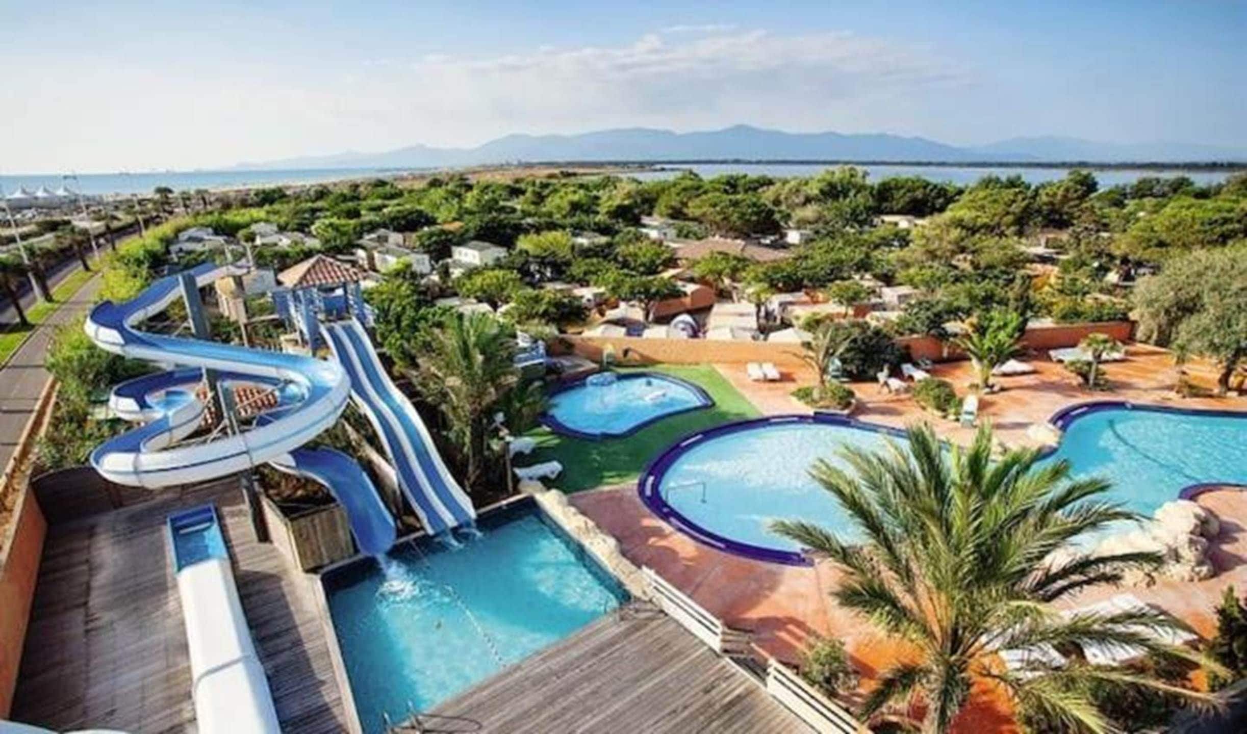 A resort with multiple swimming pools, a water slide, and a view of mountains in the distance.