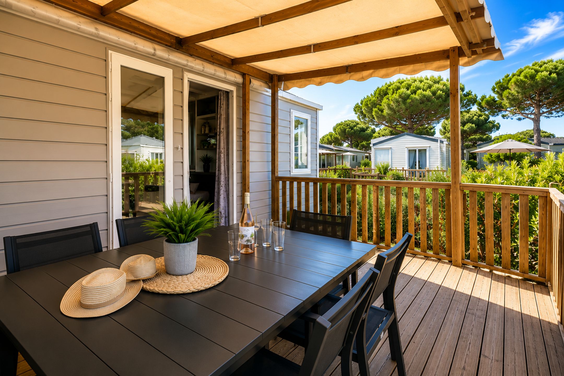 A covered outdoor dining area with a table set for two, a potted plant, and a bottle of wine.