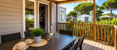 A covered outdoor dining area with a table set for two, a potted plant, and a bottle of wine.