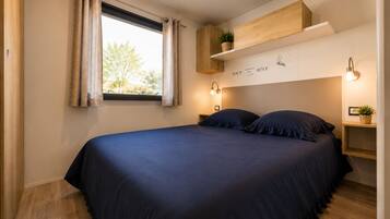 Ein Schlafzimmer mit Bett, Vorhängen, einem Fenster, einem Regal mit Pflanze und Wandleuchten.