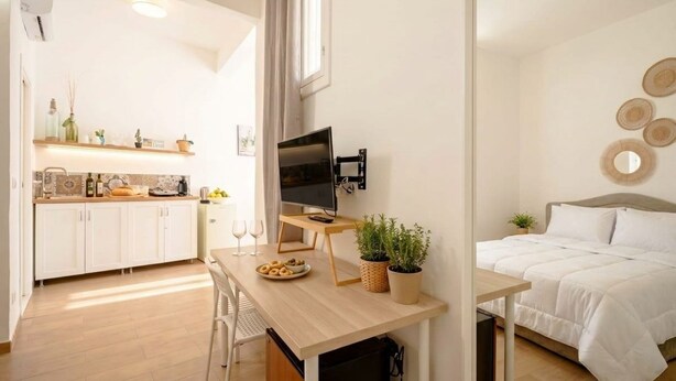 Habitación compacta con kitchenette, comedor, cama y televisor.