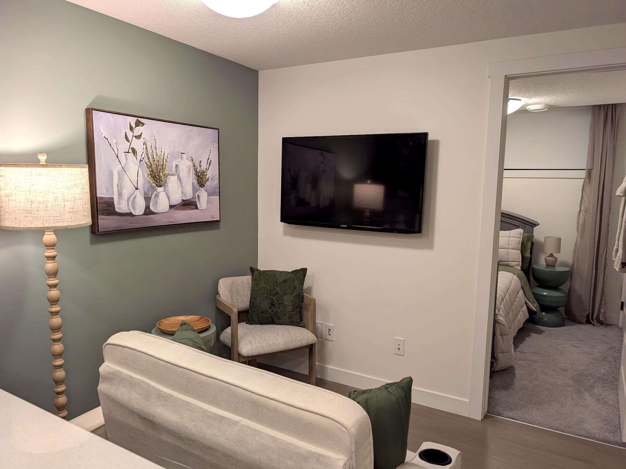 Una sala de estar moderna con una televisión de pantalla plana, un cuadro, una lámpara, un sofá y una silla.
