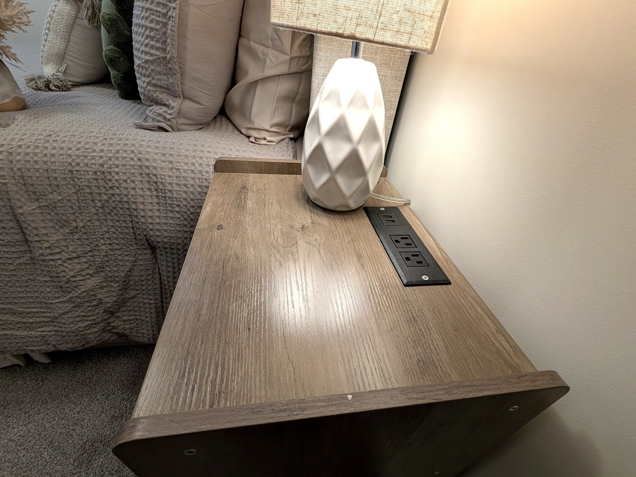 Een houten nachtkastje met een lamp en een stekkerdoos.