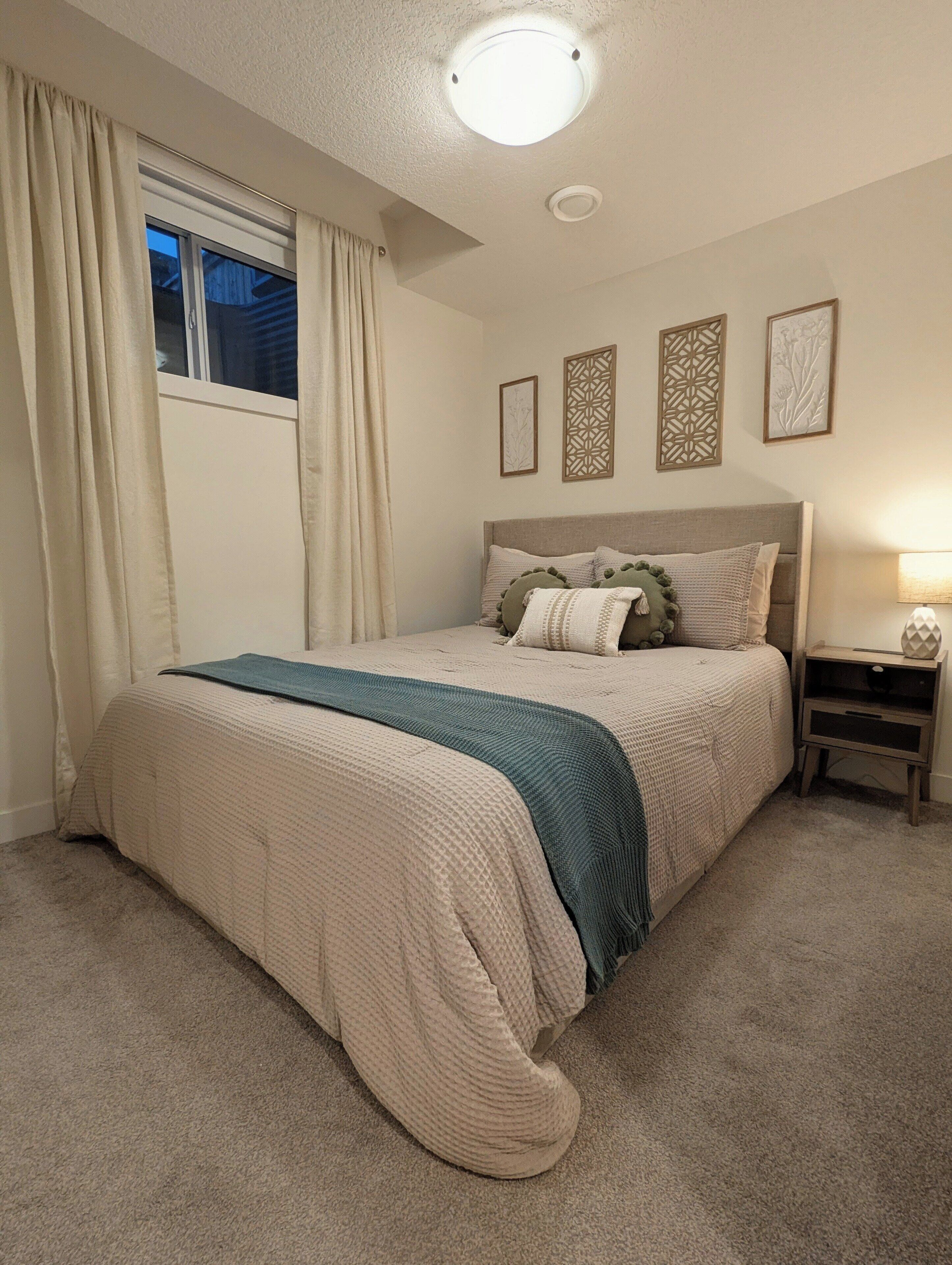 Un dormitorio con cama, mesita de noche, ventana con cortinas y adornos en la pared.