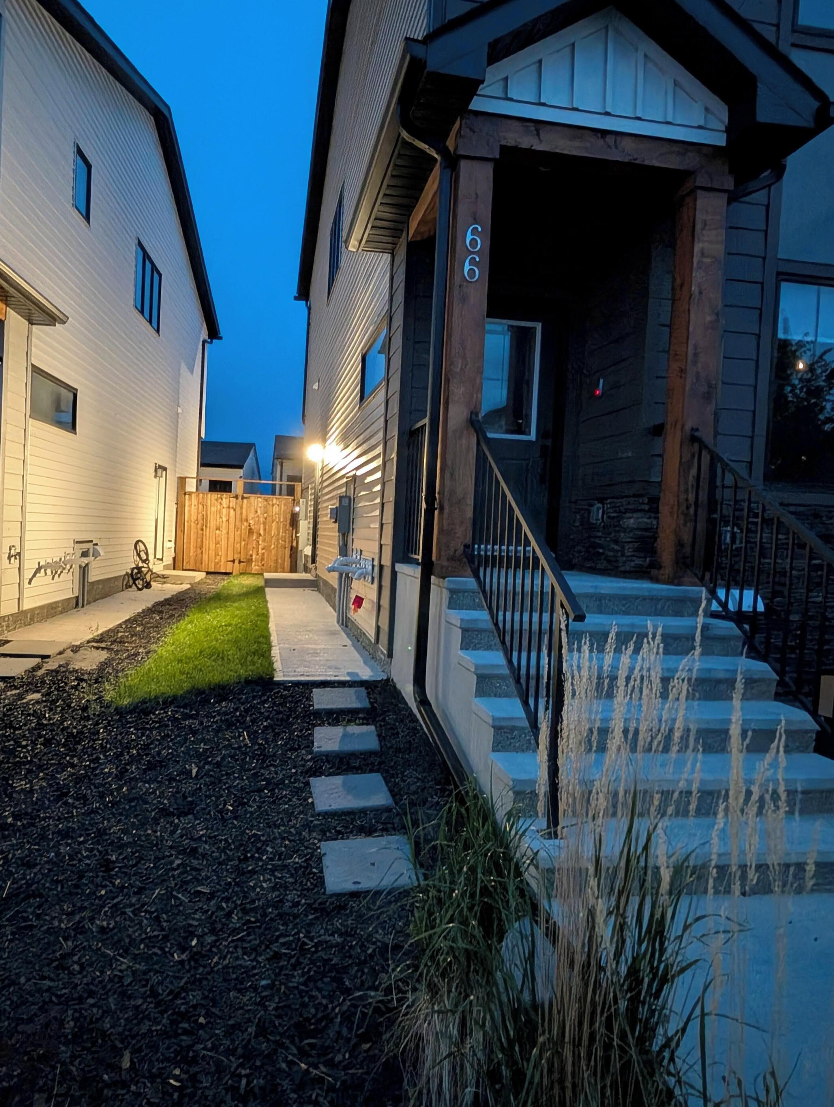 A residential building with a well-maintained lawn, a wooden fence, and a stone staircase leading to the entrance.
