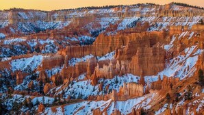 Ein weitreichender Blick auf eine zerklüftete Canyonlandschaft mit schneebedeckten Gipfeln und wolkenlosem Himmel.