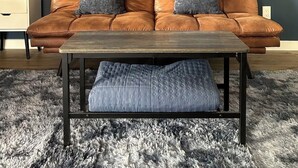 Ein Wohnzimmer mit einem braunen Ledersofa, einem Holztisch, einem grauen Teppich und einer Wandregal mit Dekoration.