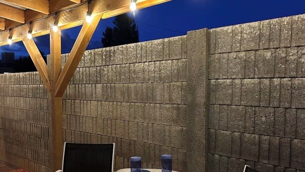Ein Sitzbereich im Freien mit zwei Stühlen und einem Tisch, unter einer Hollaube mit Lichterketten.