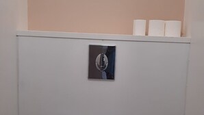 Um banheiro pequeno e compacto com vaso sanitário branco, descarga, garrafa de água azul e escova de limpeza preta.