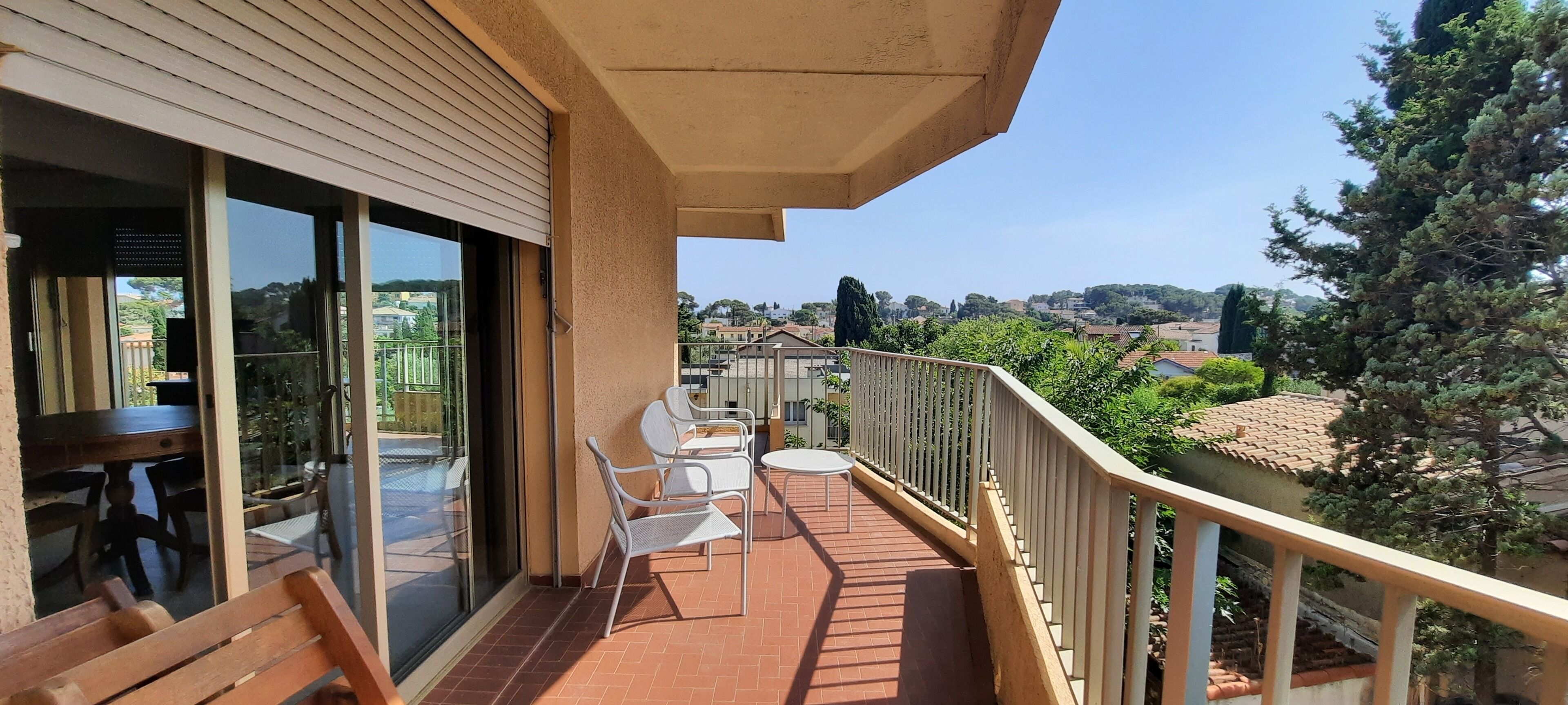 A balcony with a table and chairs, a view of the surrounding area, and a railing.